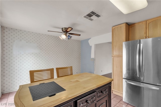 kitchen featuring light tile patterned floors, visible vents, a ceiling fan, freestanding refrigerator, and wallpapered walls