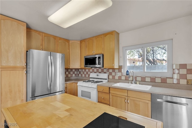 kitchen featuring appliances with stainless steel finishes, light brown cabinets, a sink, and backsplash