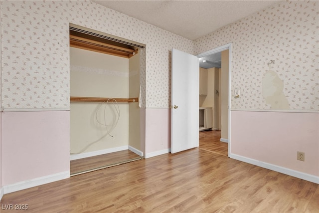 unfurnished bedroom with wood finished floors, a textured ceiling, baseboards, and wallpapered walls