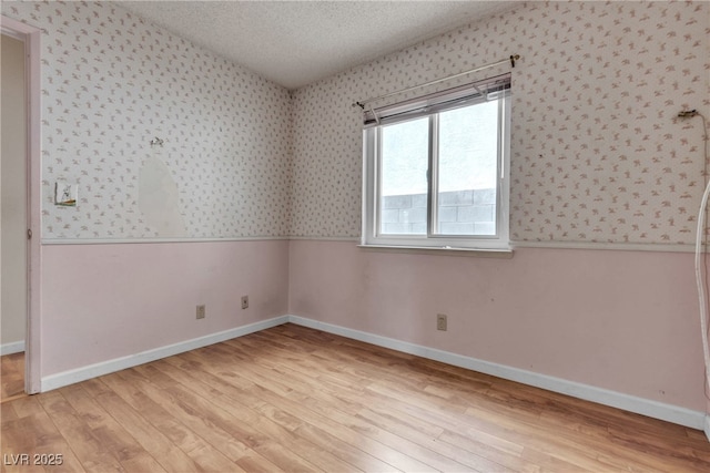 spare room featuring wallpapered walls, light wood-style flooring, baseboards, and a textured ceiling