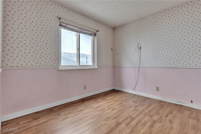 spare room featuring a textured ceiling, light wood-style floors, wainscoting, and wallpapered walls