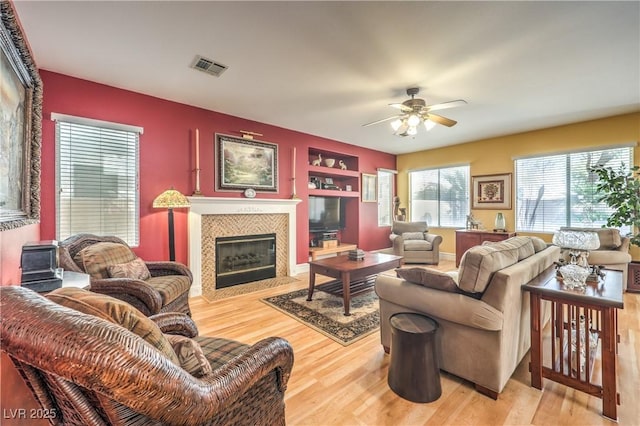 living area featuring ceiling fan, light wood-type flooring, a tile fireplace, and visible vents