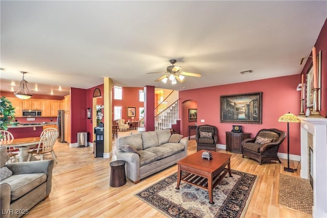 living area featuring visible vents, baseboards, a fireplace with flush hearth, stairway, and light wood-style floors