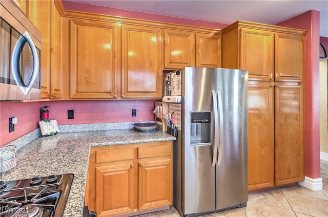 kitchen featuring stainless steel appliances, light tile patterned flooring, brown cabinetry, and light stone countertops