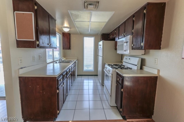 kitchen featuring dark brown cabinetry, sink, light tile patterned floors, and white appliances