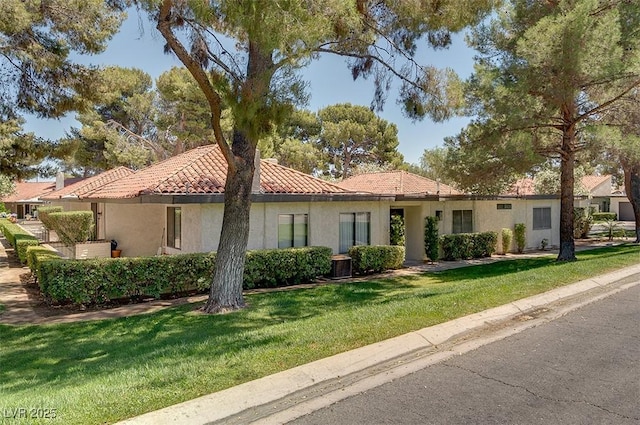 mediterranean / spanish-style home with a front lawn, a tiled roof, central AC, and stucco siding