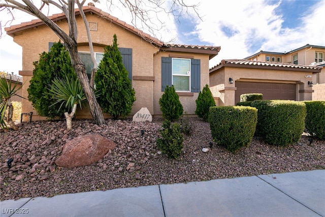 mediterranean / spanish home featuring stucco siding, a tiled roof, and an attached garage