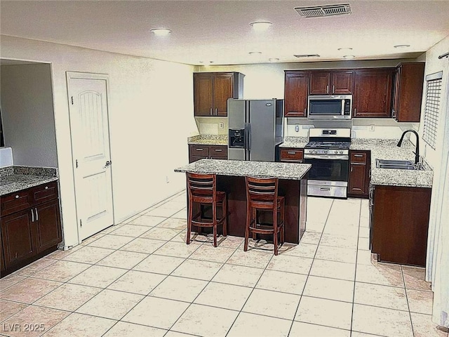 kitchen with a kitchen island, appliances with stainless steel finishes, sink, a kitchen bar, and dark brown cabinets