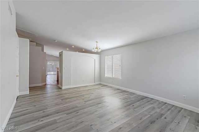 spare room featuring light wood-style flooring, baseboards, and a notable chandelier