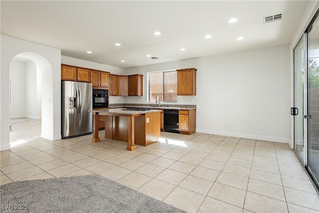 kitchen featuring a kitchen bar, a center island, black appliances, a healthy amount of sunlight, and light tile patterned flooring