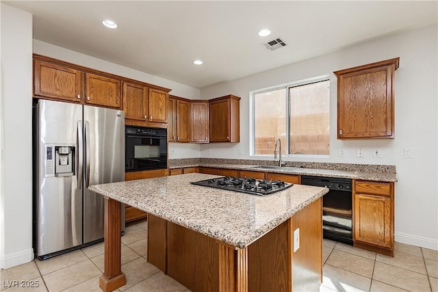 kitchen with sink, light tile patterned floors, a center island, black appliances, and light stone countertops