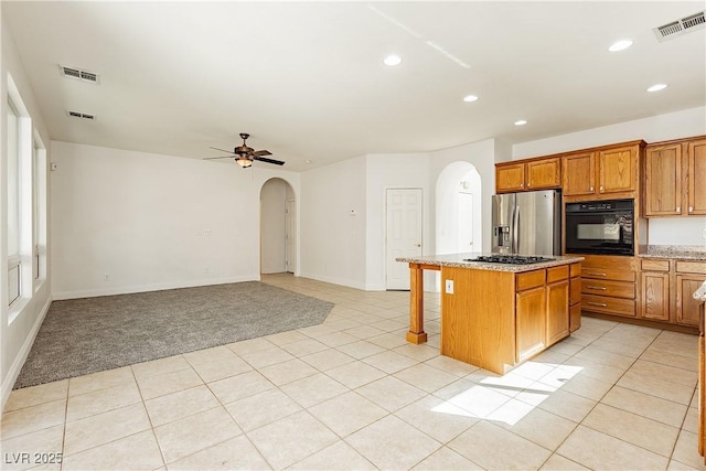 kitchen featuring light tile patterned flooring, black oven, stainless steel fridge, a kitchen breakfast bar, and a center island