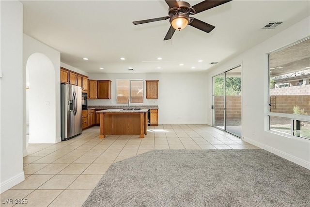 kitchen featuring light tile patterned flooring, sink, a center island, stainless steel fridge, and ceiling fan