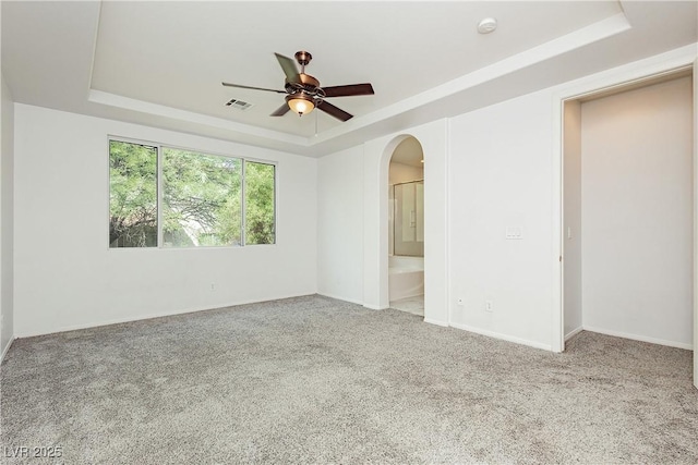 unfurnished bedroom featuring carpet flooring, connected bathroom, ceiling fan, and a tray ceiling