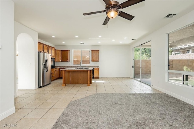 kitchen with light tile patterned floors, a center island, stainless steel refrigerator with ice dispenser, visible vents, and brown cabinetry