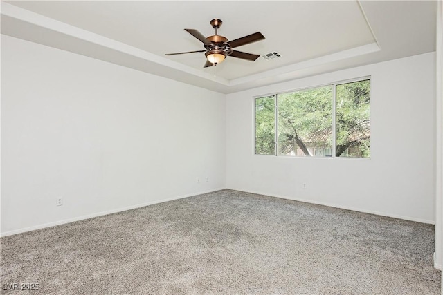 carpeted spare room with visible vents, ceiling fan, a raised ceiling, and baseboards