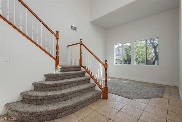 stairs featuring tile patterned floors, a high ceiling, baseboards, and visible vents