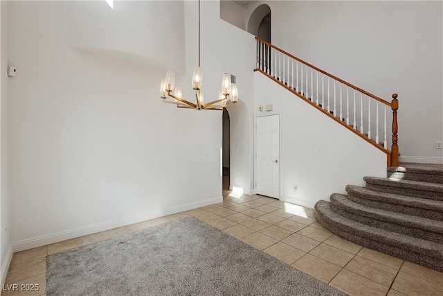 interior space featuring arched walkways, a towering ceiling, tile patterned floors, baseboards, and a notable chandelier