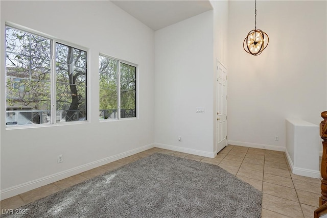 empty room featuring light tile patterned floors, baseboards, a notable chandelier, and a high ceiling