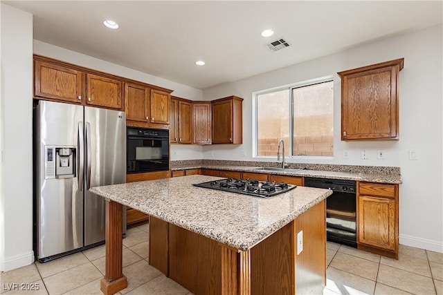 kitchen featuring visible vents, a center island, a sink, brown cabinetry, and black appliances
