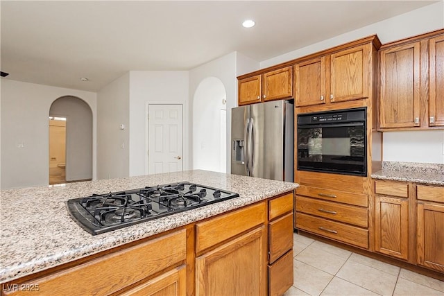 kitchen featuring arched walkways, brown cabinets, light tile patterned floors, and black appliances