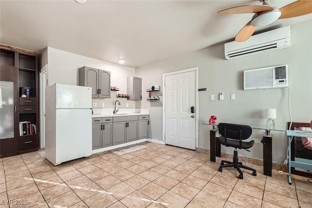 kitchen featuring light countertops, gray cabinetry, freestanding refrigerator, an AC wall unit, and a sink