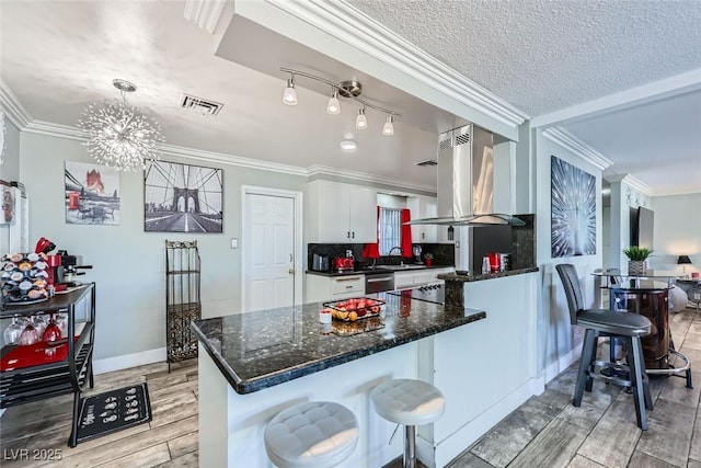 kitchen featuring visible vents, decorative light fixtures, island exhaust hood, crown molding, and white cabinetry