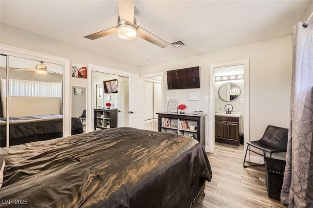 bedroom with a sink, a ceiling fan, light wood-style floors, visible vents, and multiple closets