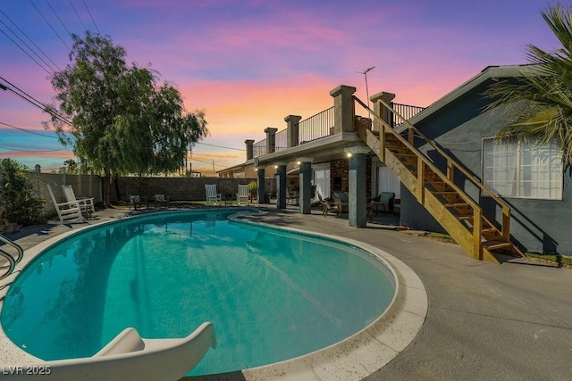 pool at dusk featuring a patio, a water slide, fence private yard, stairway, and a fenced in pool