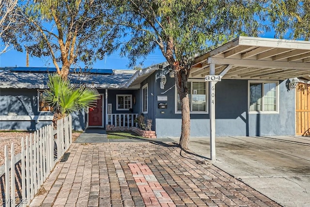 entrance to property with roof mounted solar panels, fence, and stucco siding