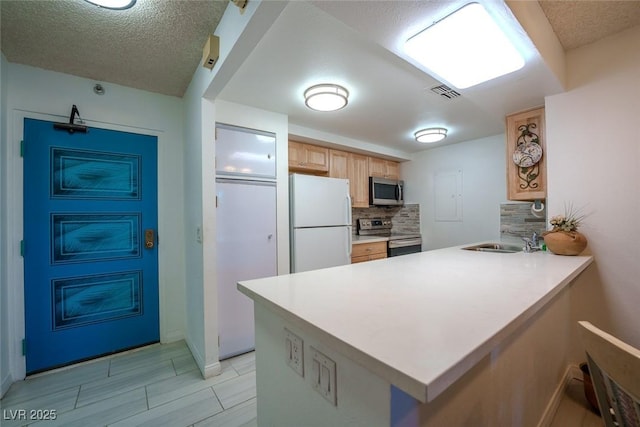 kitchen featuring sink, appliances with stainless steel finishes, a textured ceiling, decorative backsplash, and kitchen peninsula