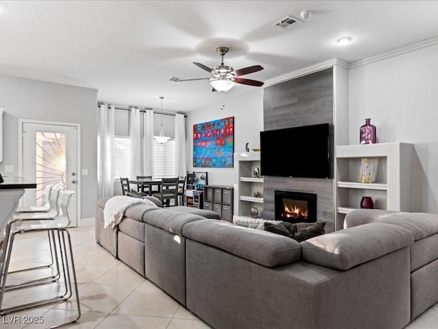 tiled living room featuring crown molding, a large fireplace, and ceiling fan