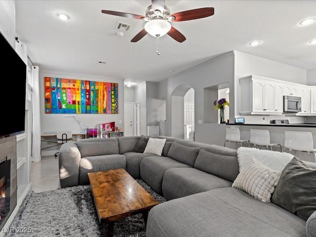 living room with ceiling fan, ornamental molding, and light tile patterned floors