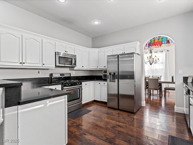 kitchen with appliances with stainless steel finishes, dark wood-type flooring, white cabinets, and an inviting chandelier