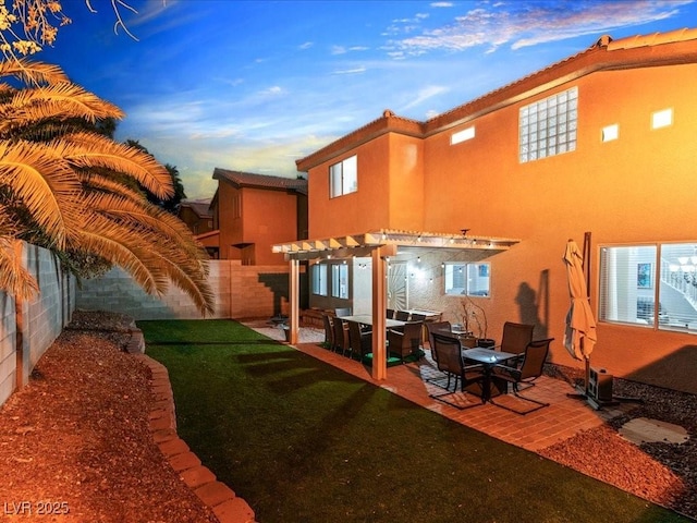 back house at dusk featuring a pergola, a patio, and a lawn