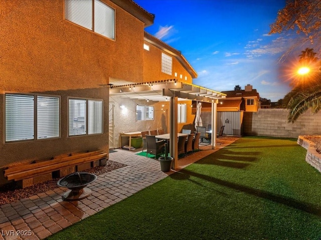 back house at dusk with a pergola, a lawn, an outdoor fire pit, and a patio area