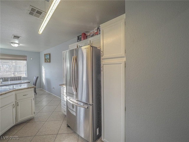 kitchen with white cabinetry, light tile patterned floors, stainless steel refrigerator, and a textured ceiling