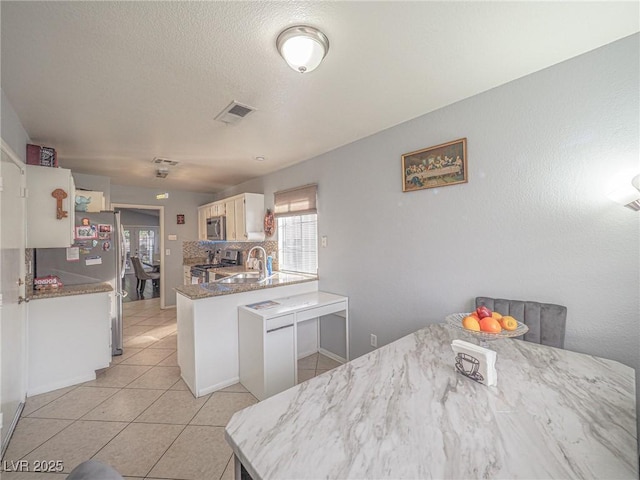 kitchen featuring sink, light tile patterned floors, appliances with stainless steel finishes, kitchen peninsula, and white cabinets