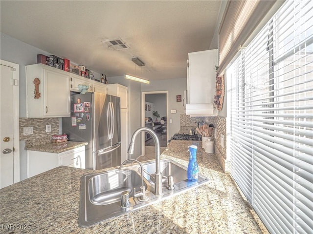 kitchen with white cabinets, tasteful backsplash, sink, and stainless steel fridge