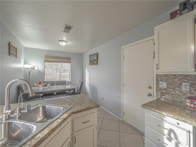 kitchen featuring sink, light tile patterned floors, a textured ceiling, white cabinets, and decorative backsplash