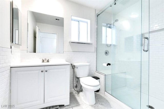 bathroom with tile walls, tile patterned flooring, vanity, toilet, and walk in shower