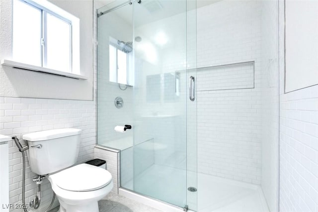 bathroom with walk in shower, toilet, and tile walls