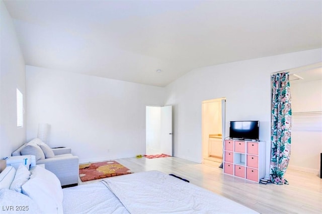 bedroom featuring light hardwood / wood-style flooring, a walk in closet, vaulted ceiling, and ensuite bath