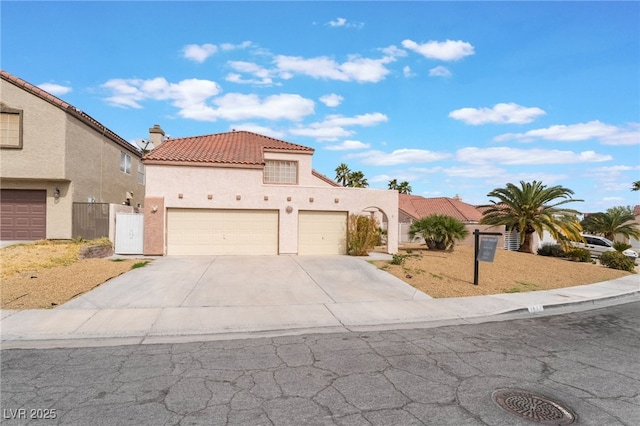 mediterranean / spanish-style home featuring a tile roof, stucco siding, a chimney, driveway, and an attached garage