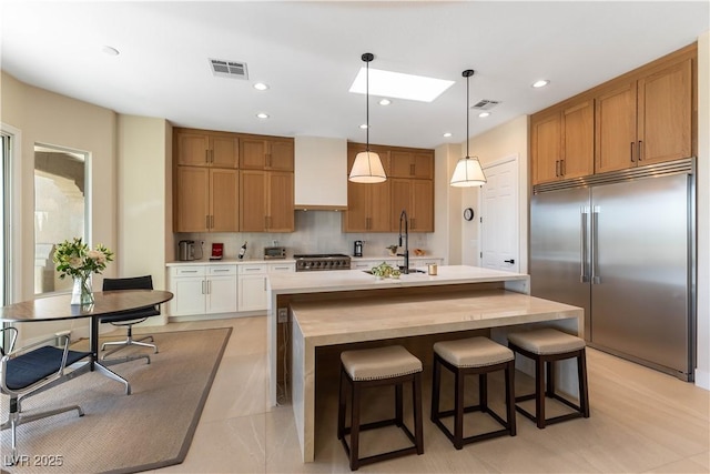 4796 Riva De Romanza St, Las Vegas, NV 89135 - kitchen with high end appliances, light countertops, a skylight, a center island with sink, and brown cabinets