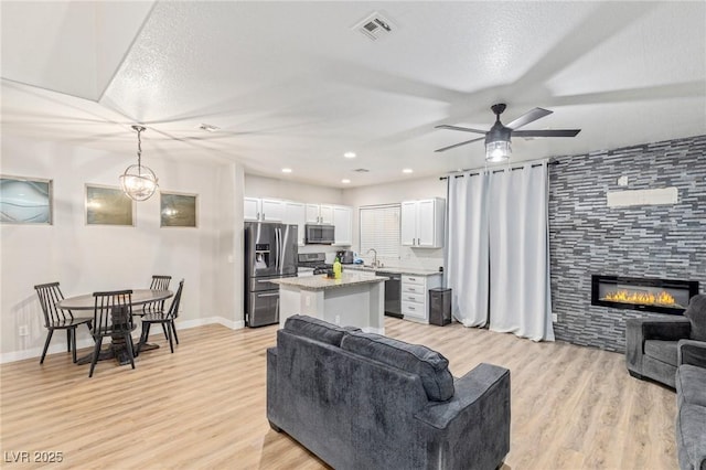 living room featuring ceiling fan, light hardwood / wood-style floors, a tile fireplace, and a textured ceiling