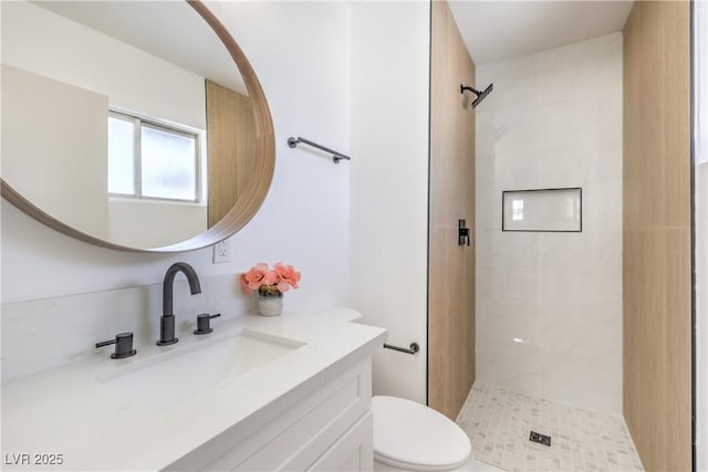 bathroom featuring toilet, a tile shower, and vanity