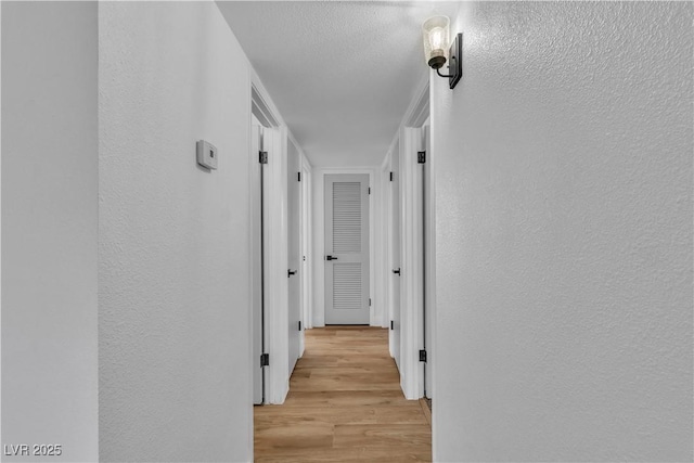 hallway featuring a textured ceiling, a textured wall, and light wood-type flooring