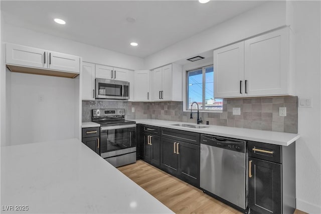 kitchen featuring stainless steel appliances, light countertops, white cabinets, a sink, and dark cabinetry