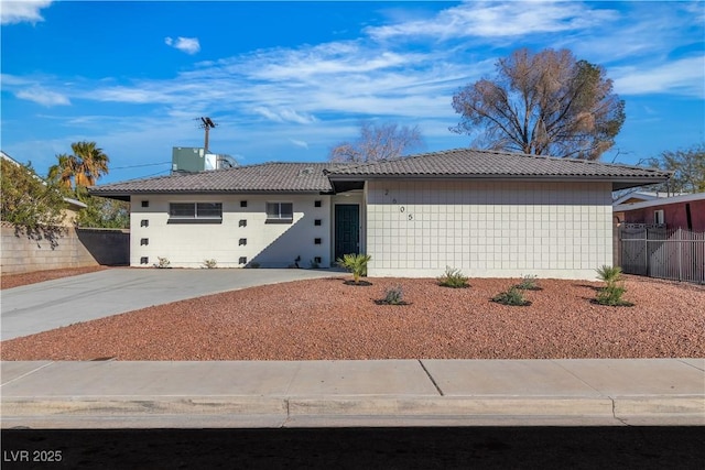 ranch-style home featuring a tiled roof, central AC unit, concrete driveway, and fence